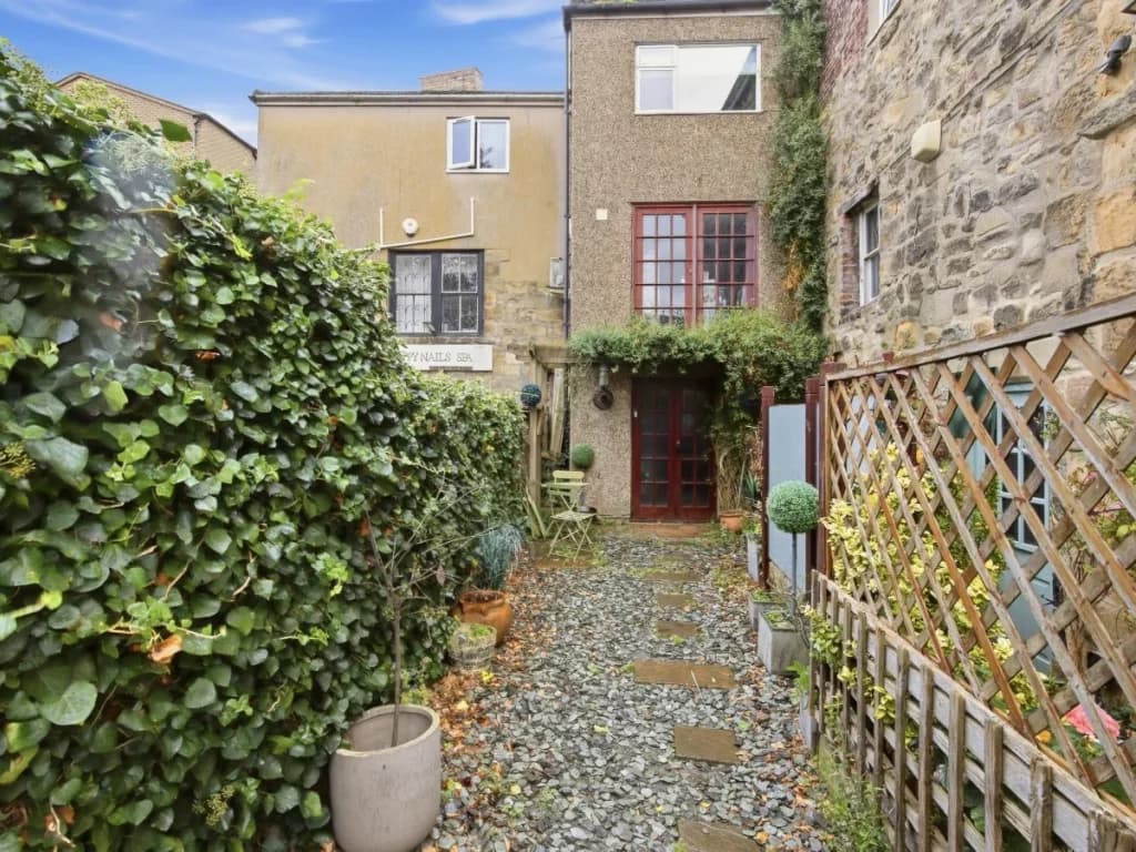 Private rear entrance framed by stone walls, greenery and garden details.