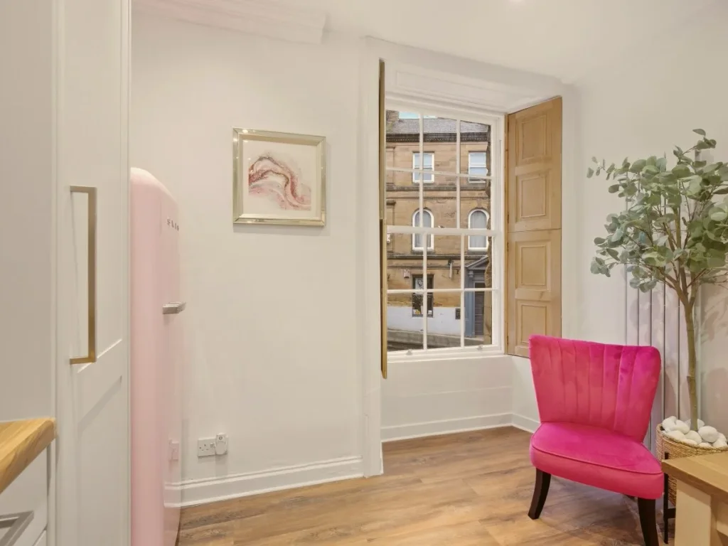 Bright kitchen corner with sash window, pink fridge and statement chair.
