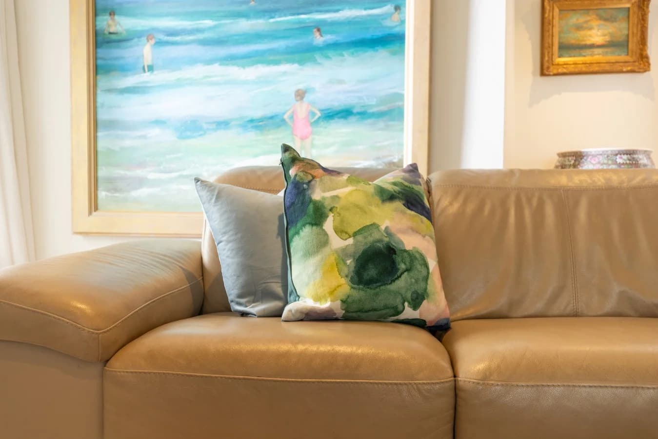 Tan leather sofa with coastal artwork and patterned cushions.