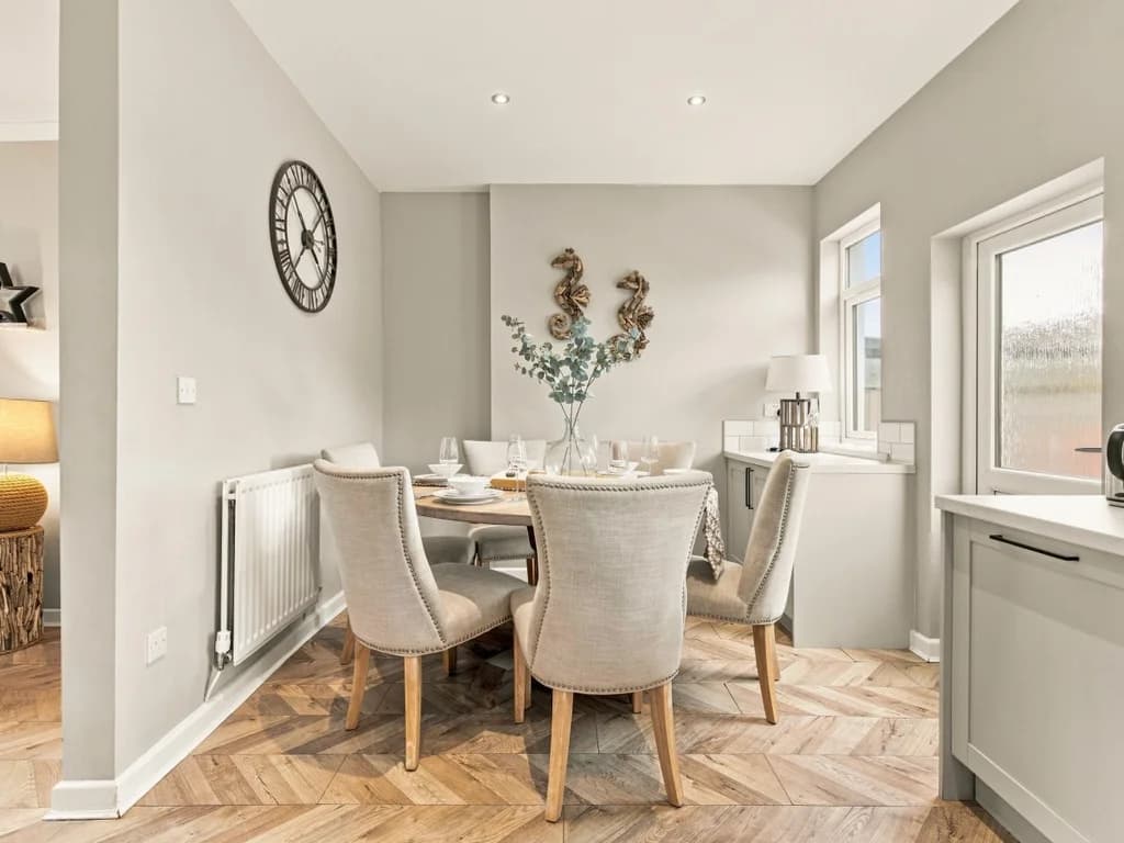 Dining area with upholstered chairs and windows overlooking the garden.