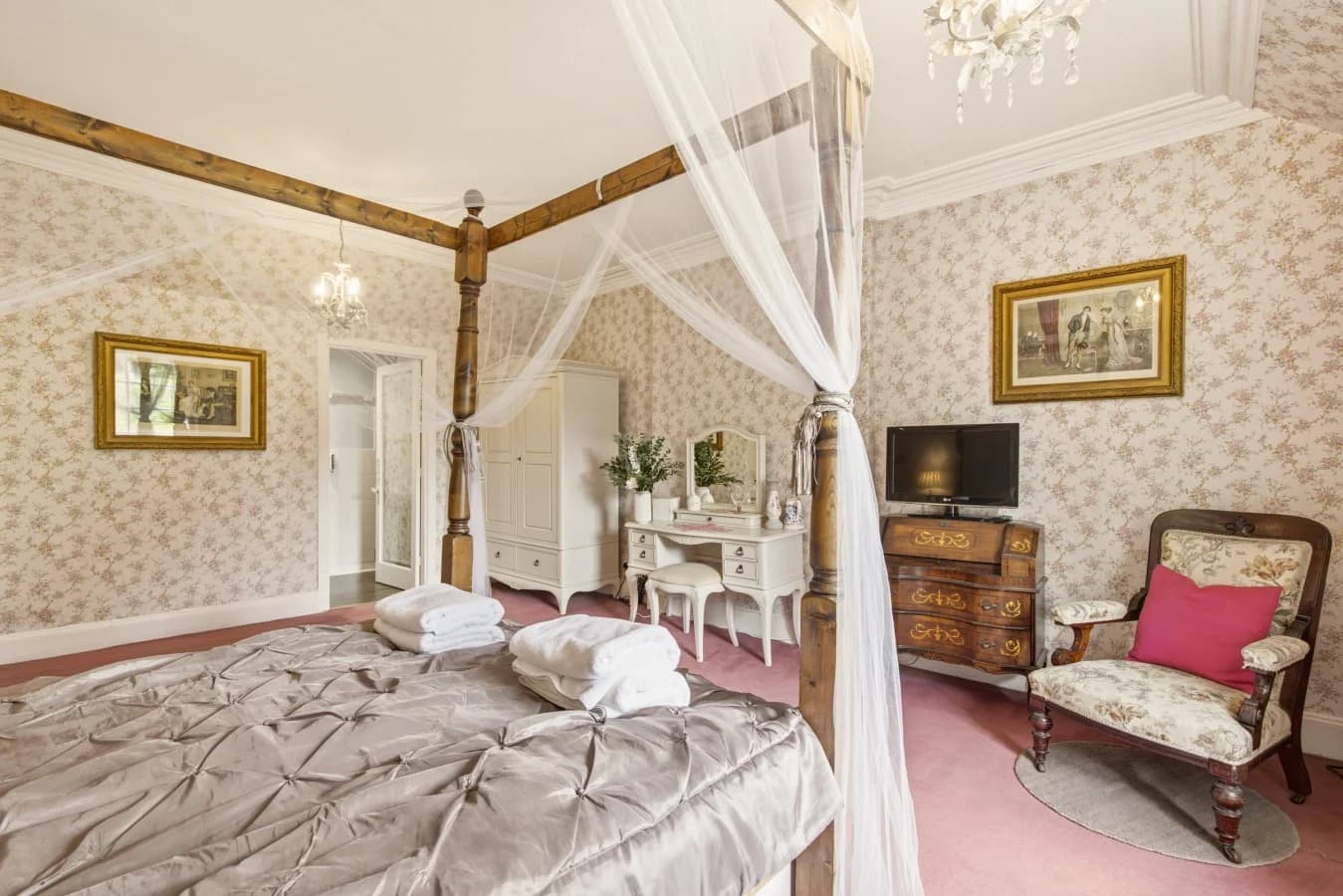 Four poster bed with dressing table, TV and floral wallpaper.