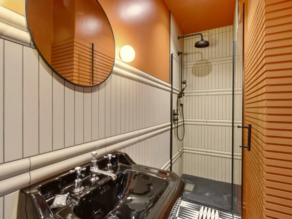 Modern shower room with walk-in shower, black basin and round mirror.