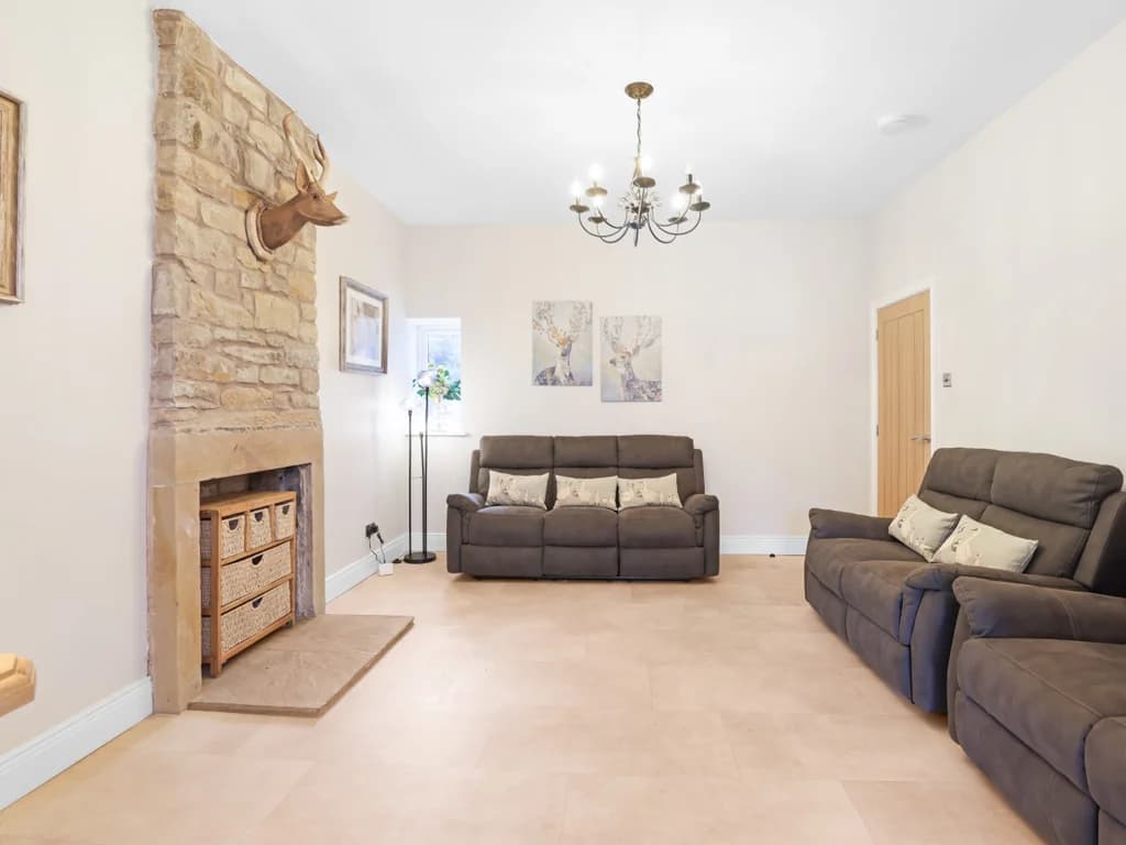 This spacious living area features neutral tones, comfortable brown sofas, and a rustic stone fireplace adorned with a mounted stag head.