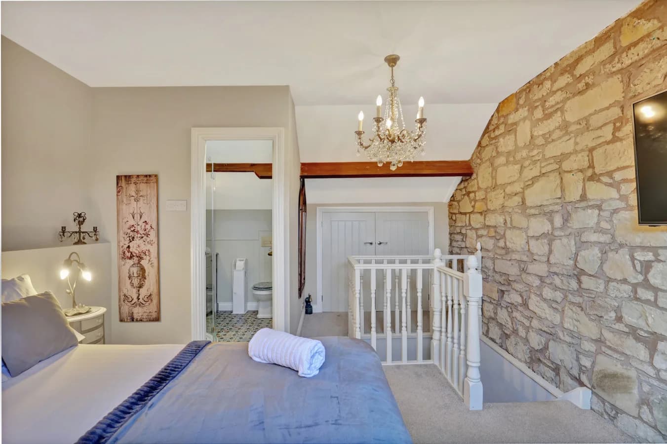 Spacious principal bedroom with exposed stone wall and landing access