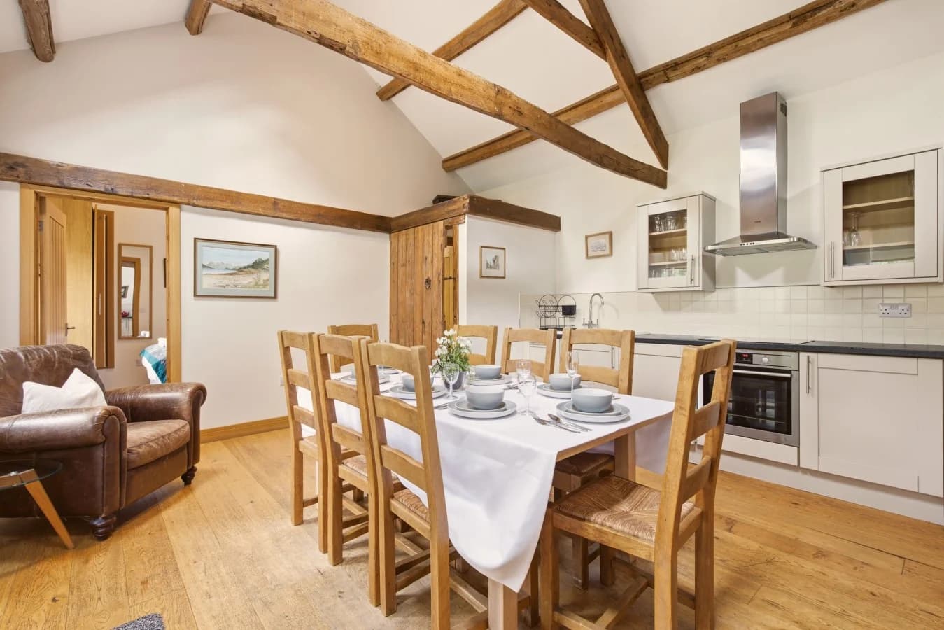 Dining table and fitted kitchen framed by exposed timber beams