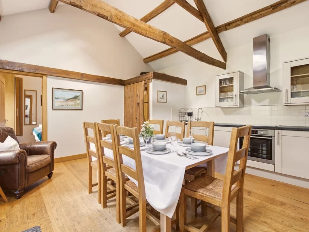 Dining table and fitted kitchen framed by exposed timber beams