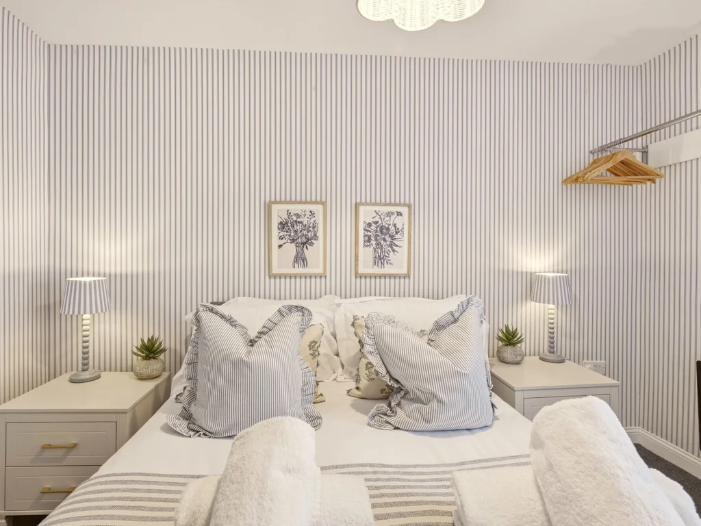Double bedroom with striped walls, bedside tables and feature lighting.