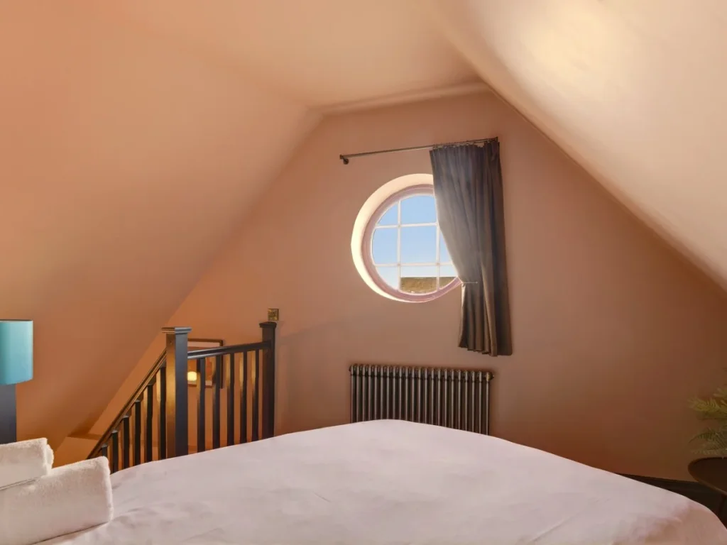 Cosy mezzanine bedroom with circular window and sloping ceilings