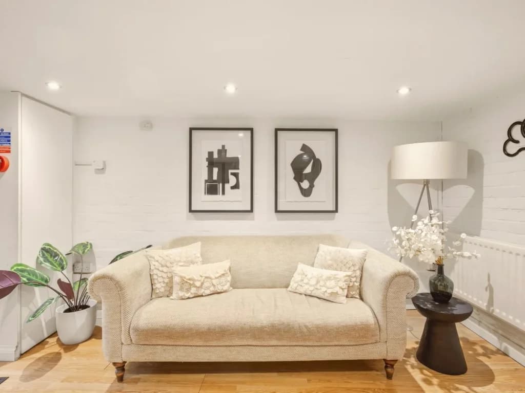 Lower living area with cream sofa, framed artwork and warm wood flooring.