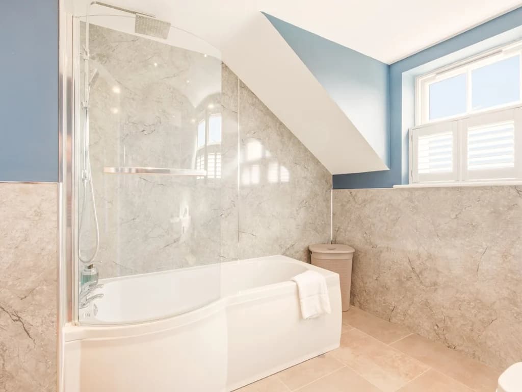 Bath with glass shower screen and natural light from shuttered window