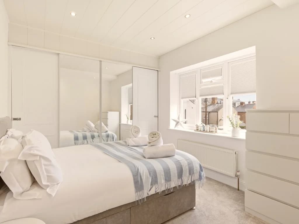 Bright double bedroom with mirrored wardrobes and large window.