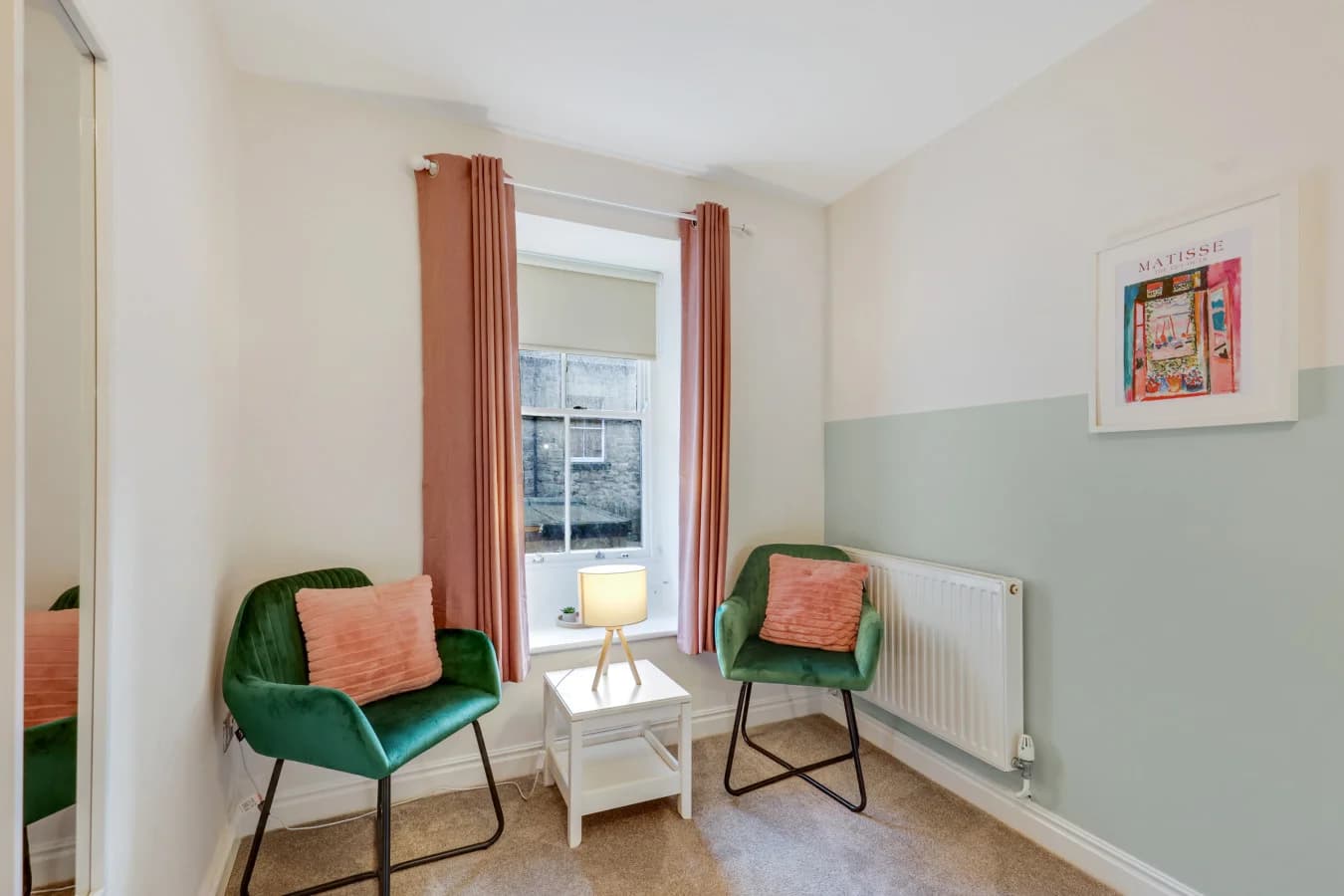 Reading nook with emerald velvet chairs beside a large sash window