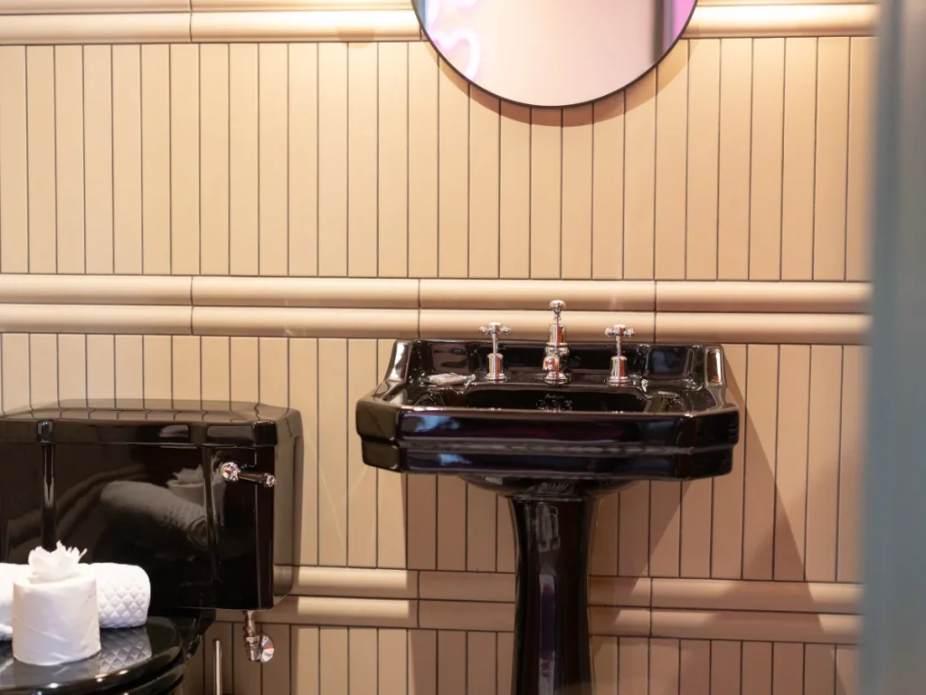Black pedestal basin with traditional taps and tiled wall detailing.