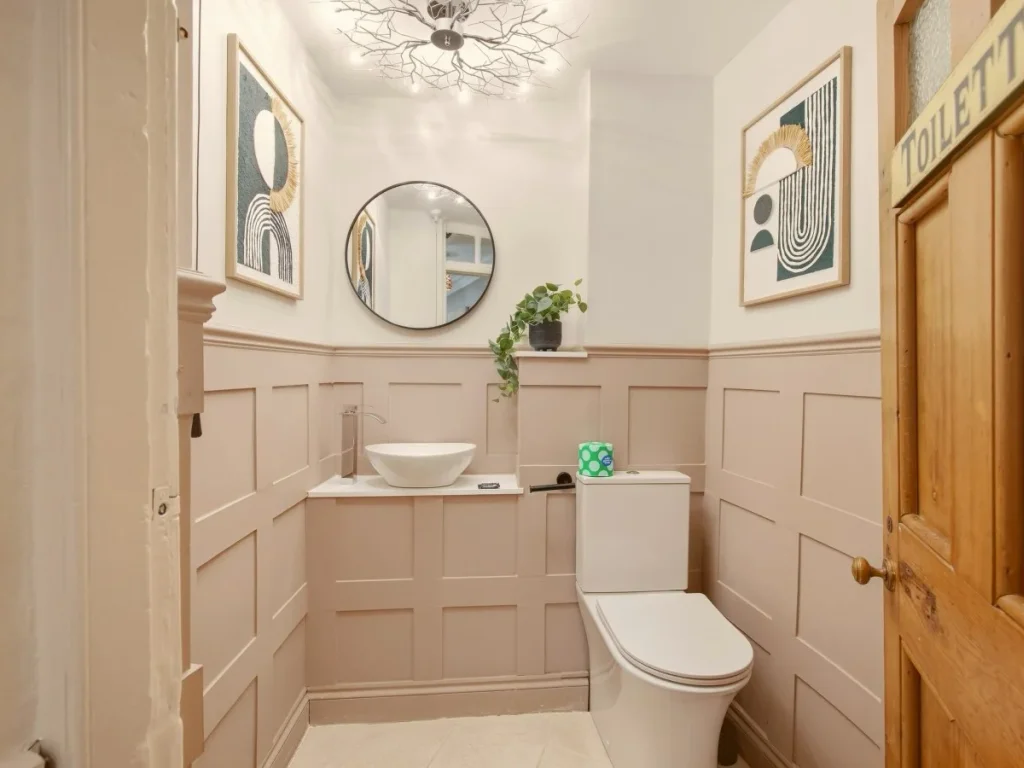 Stylish WC with panelled walls, countertop basin and round mirror.