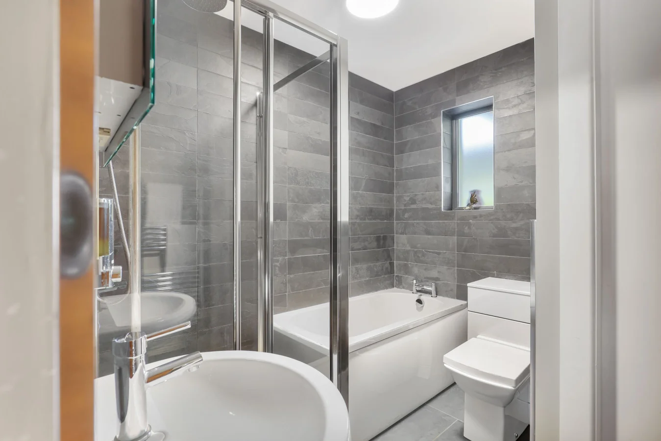 Family bathroom with bath, shower screen and grey wall tiles