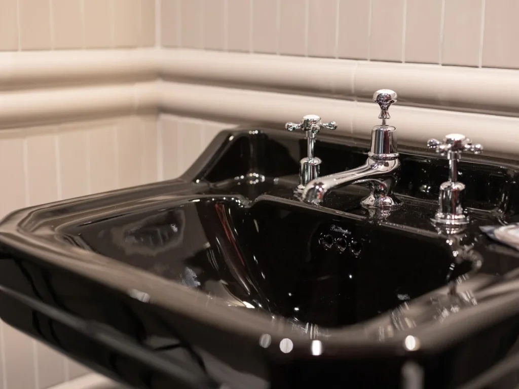 Close-up of the black basin with traditional chrome taps and tiled wall.