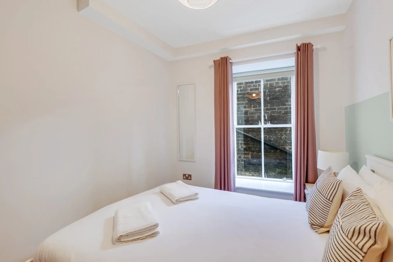 Bright double bedroom with blush-toned curtains and large sash window views