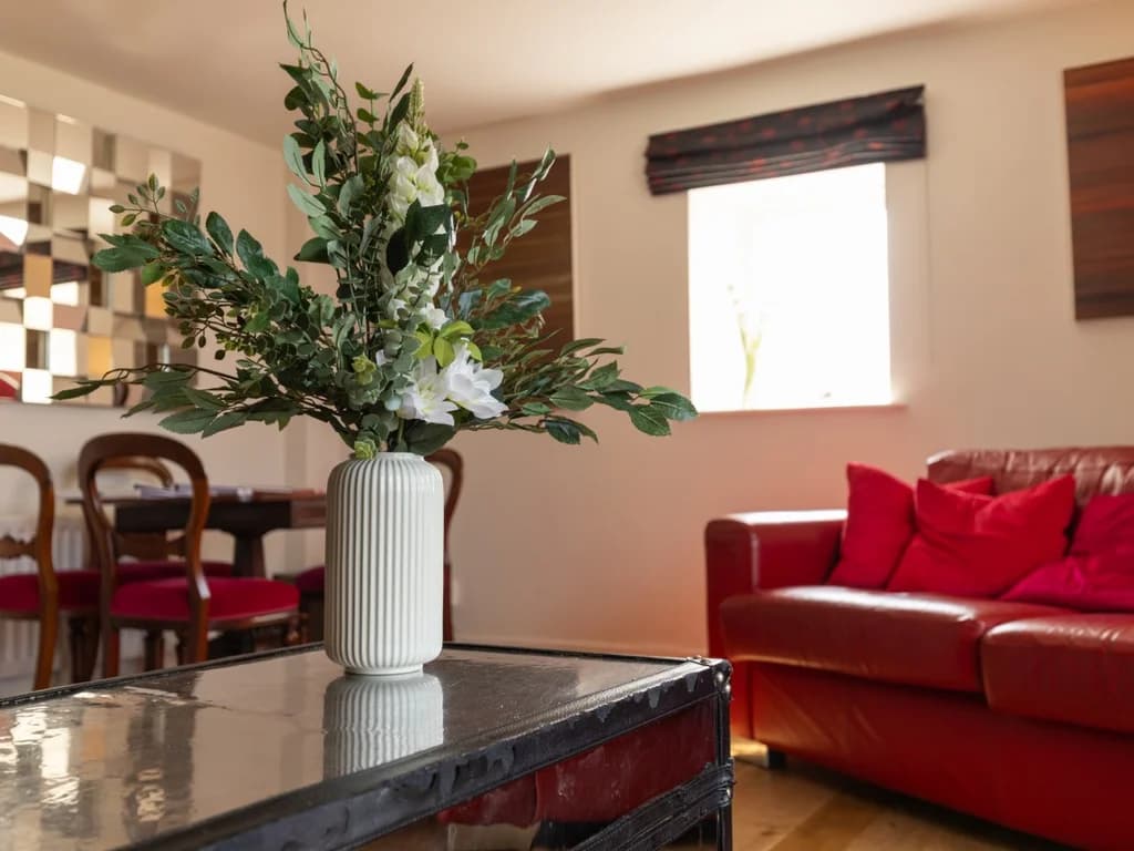 Floral arrangement with red leather sofa and dining area beyond
