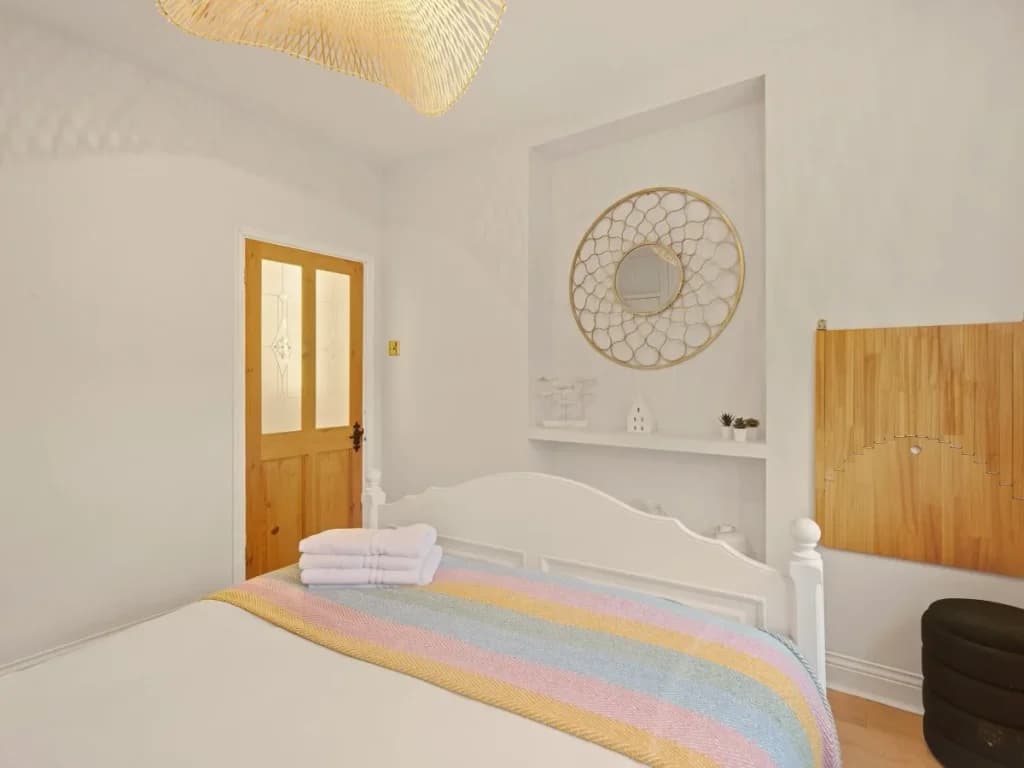 Double bedroom with pastel throw, circular mirror and warm wood details.