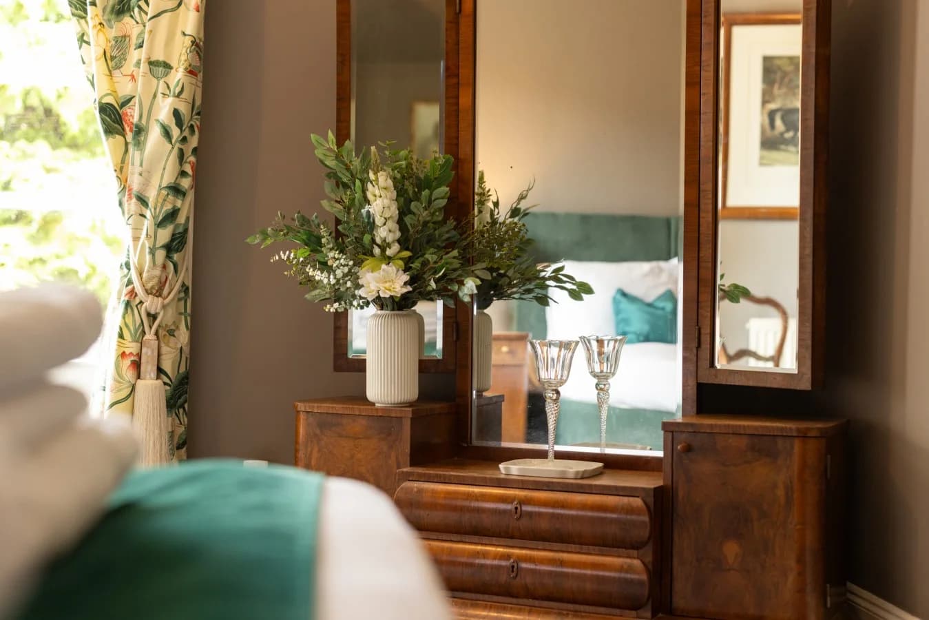 Wooden dressing table with triple mirror and fresh floral arrangement.