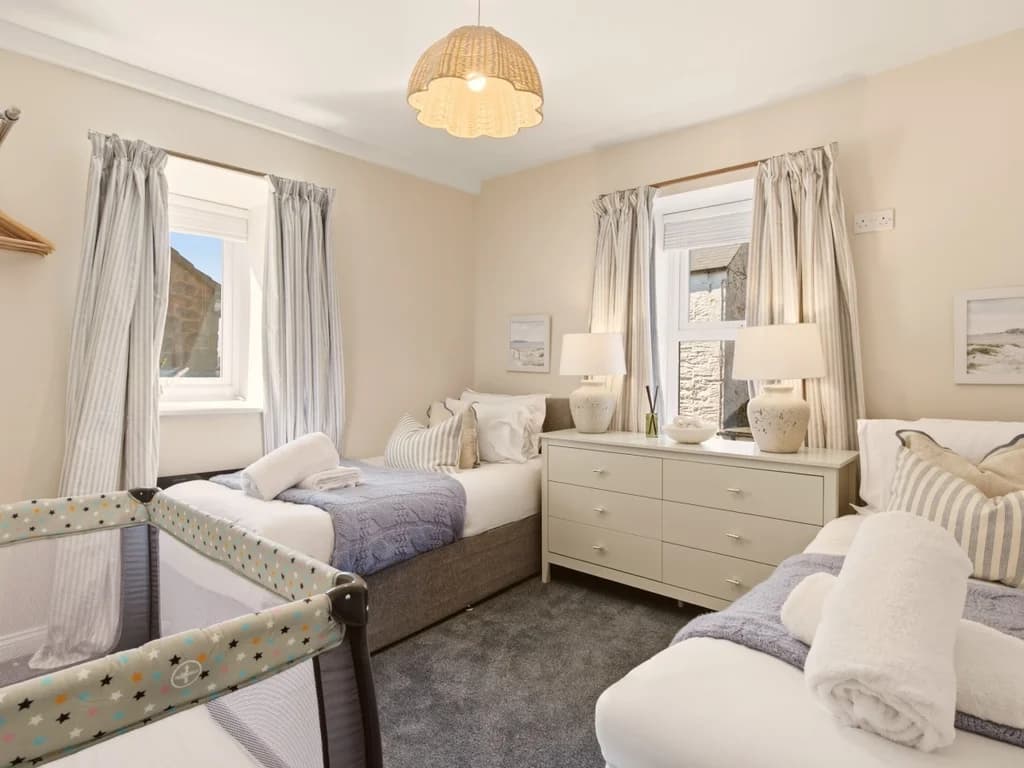 Twin bedroom with travel cot, twin beds and chest of drawers.