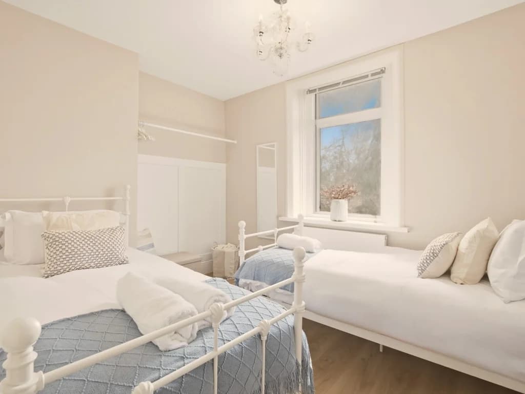 Twin bedroom with white metal beds and open clothes hanging rail