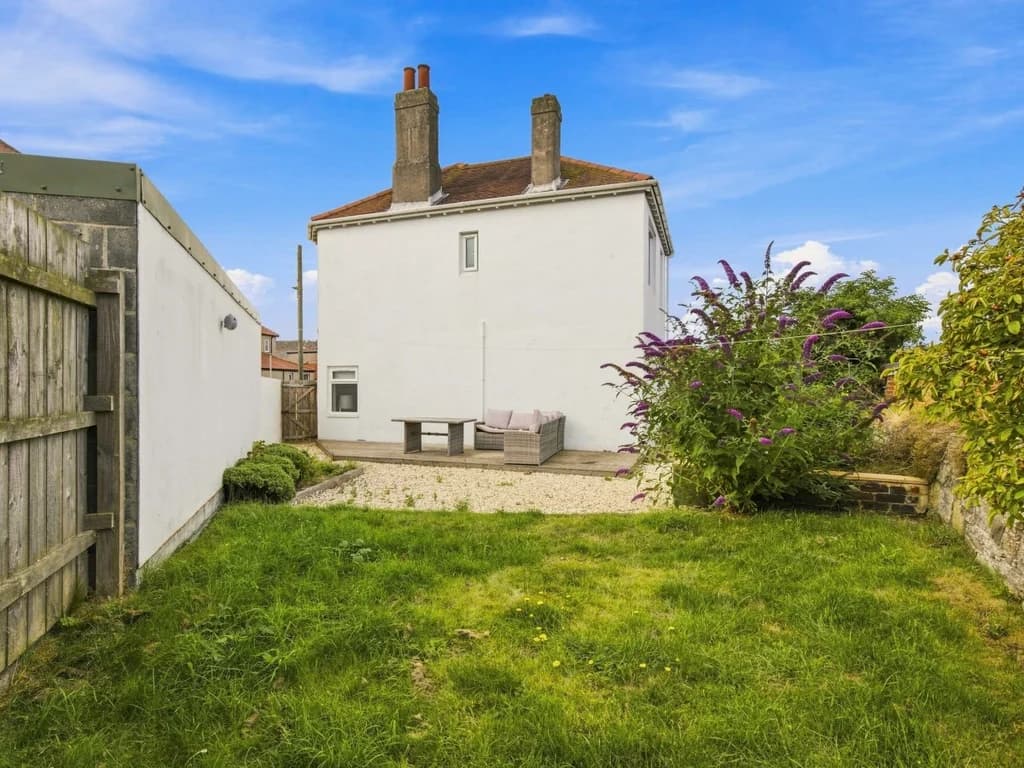 Rear garden with lawn, gravel seating area and enclosed boundaries.