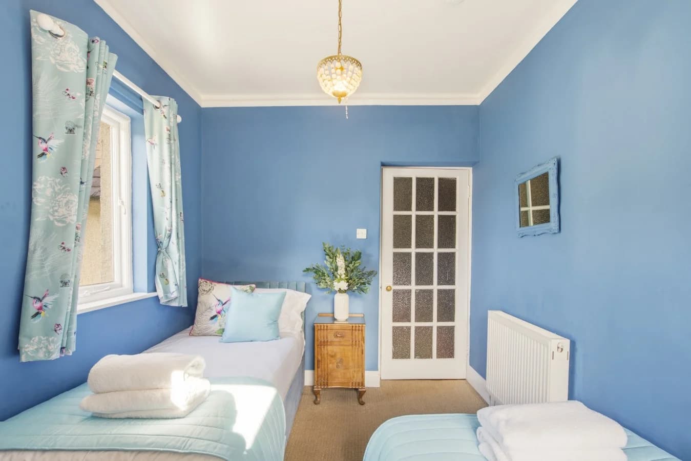 Twin bedroom with blue walls, matching beds and colourful accents