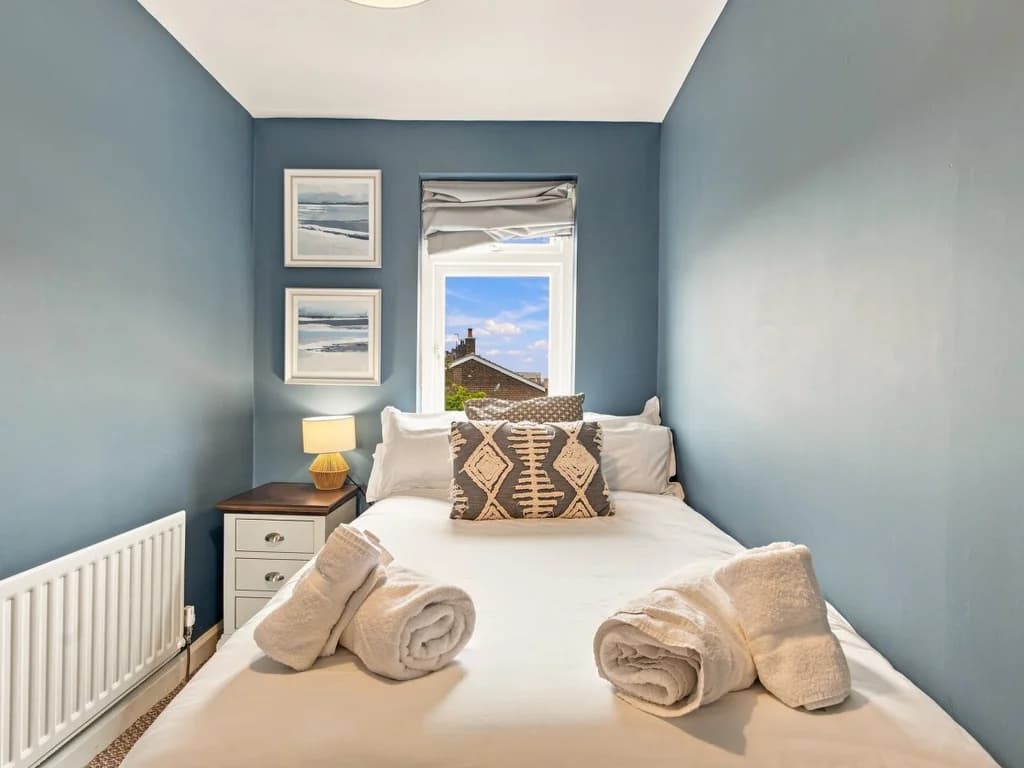 Small double bedroom with blue feature walls and framed coastal prints.