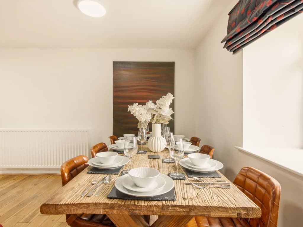 Wooden dining table with high-back leather chairs in open-plan room.