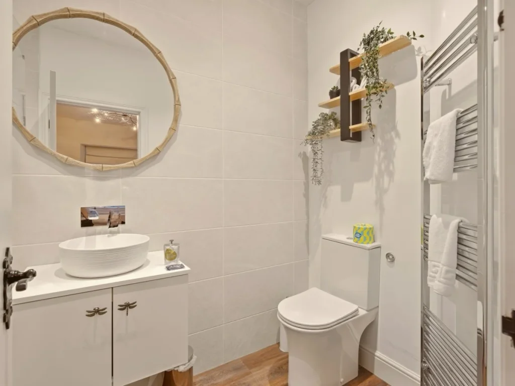 Bright ensuite with round mirror, basin, WC and heated towel rail.