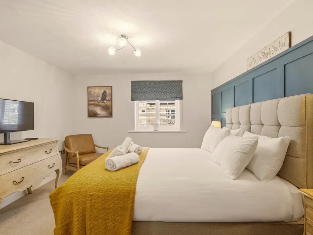 Elegant king bedroom with Smart TV, feature wall and comfortable armchair