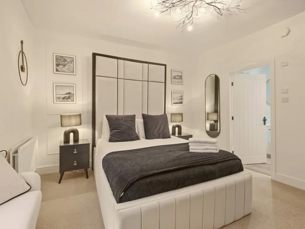 Double bedroom with upholstered bed, framed artwork and bedside lighting.