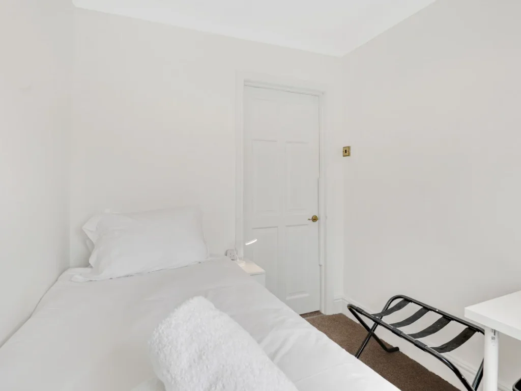 Single bedroom with luggage rack, desk and simple neutral décor