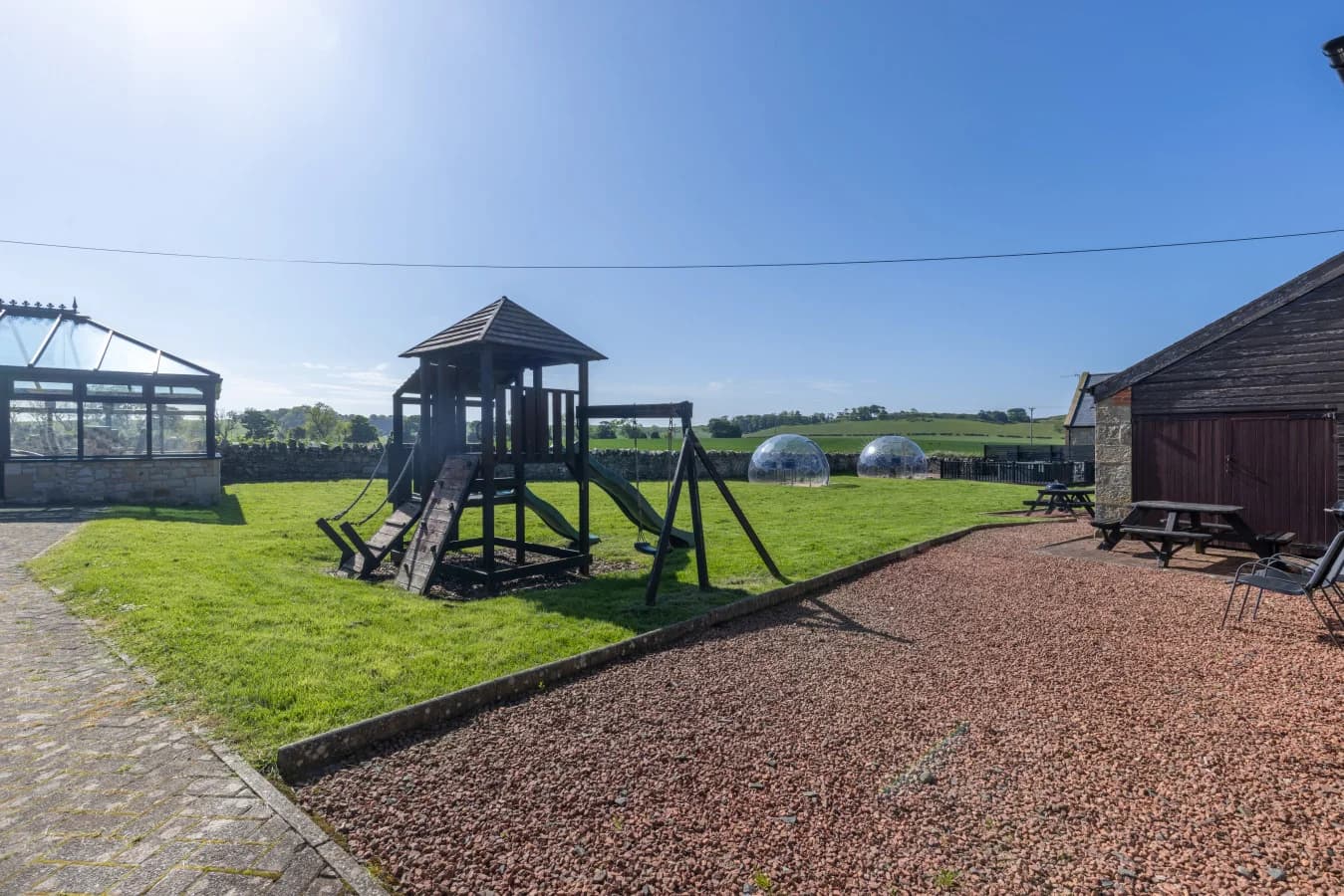 Timber play frame on a gravel courtyard and lawn