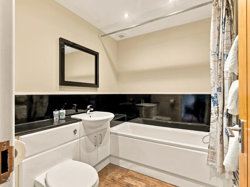 Family bathroom with bath, overhead shower and black feature tiles.