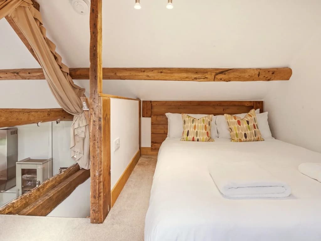 Hayloft bedroom with queen-size bed beneath exposed timber beams