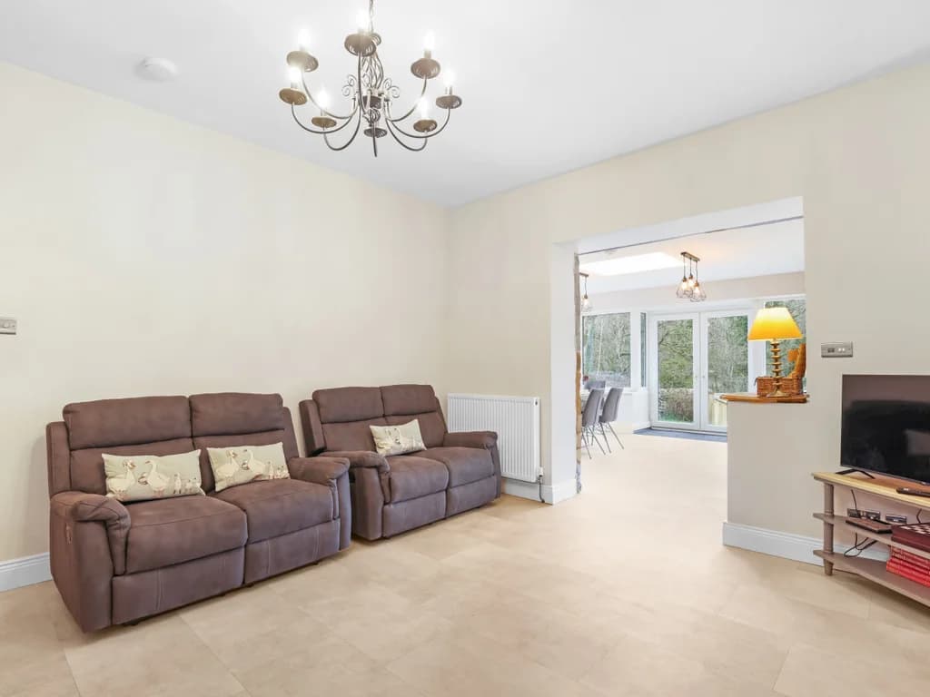 A pair of brown sofas sits opposite a television in this bright living area, which opens up into a sunlit dining space.