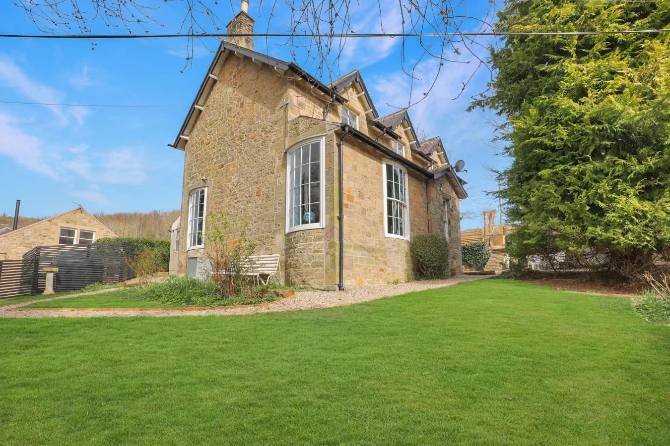 Stone-built cottage exterior with lawn, mature trees and garden borders