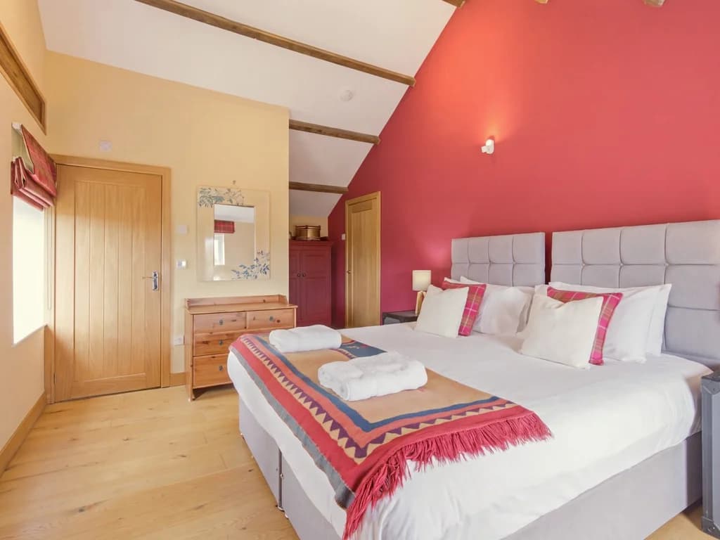 King-size bedroom with bold red feature wall and exposed beams