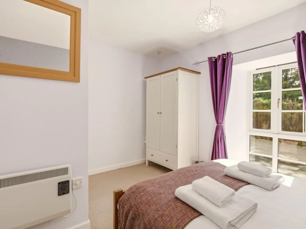 King bedroom with wardrobe, large mirror and doors overlooking greenery