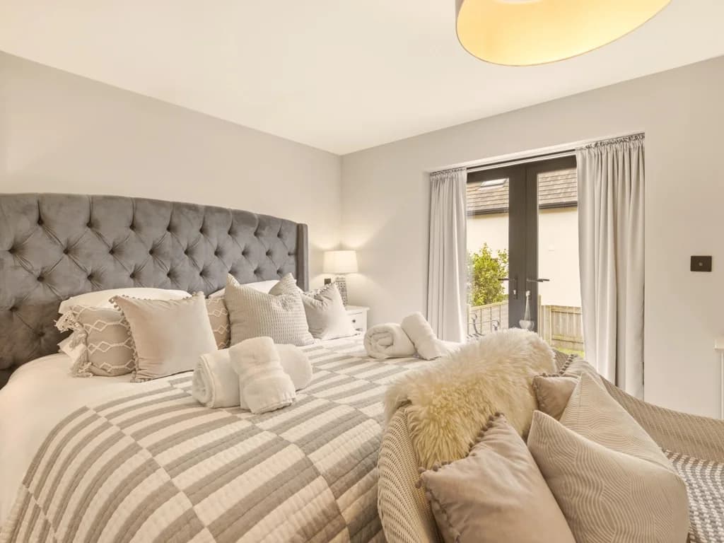 King bedroom with tufted headboard, French doors and soft neutral décor
