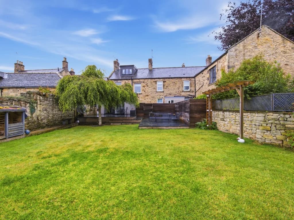 Spacious enclosed rear garden with lawn, mature trees and children's play equipment.