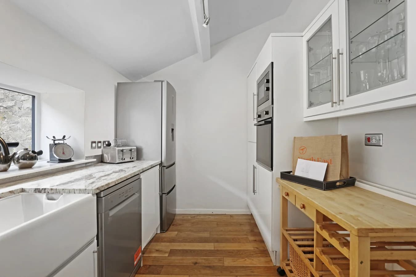 Kitchen with white cabinetry, integrated ovens and oak flooring