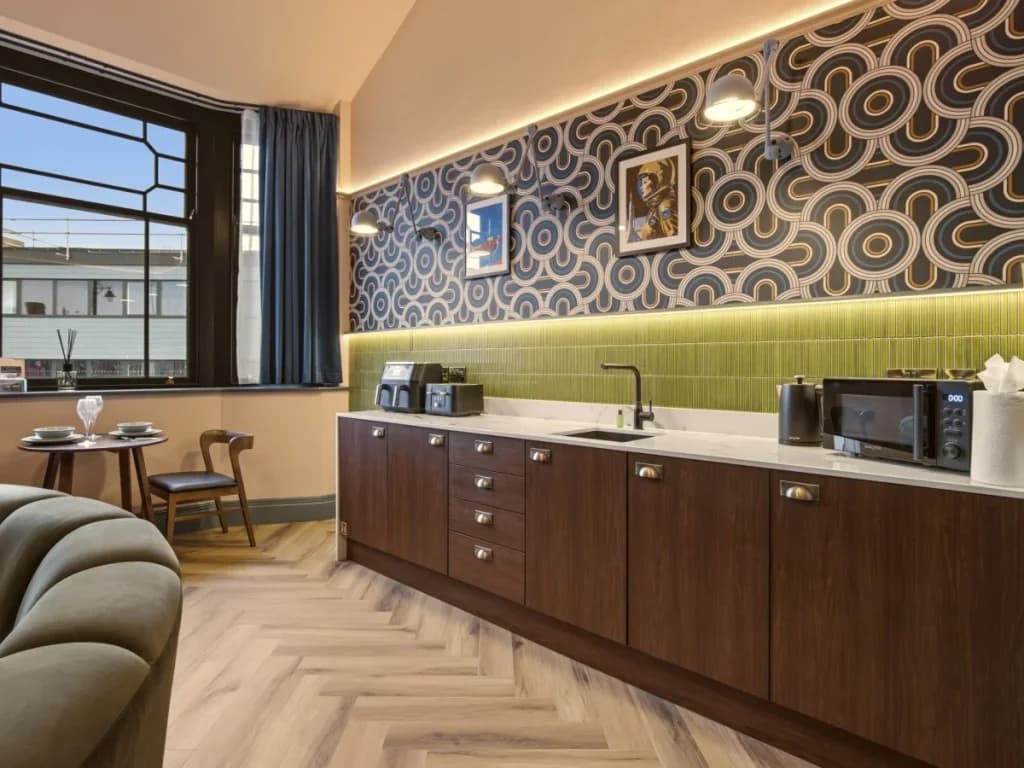 Contemporary kitchenette with wood cabinetry and illuminated green tiles.