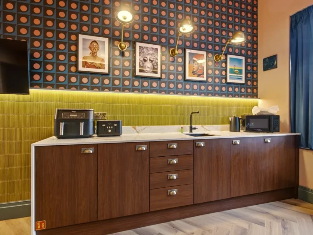 Kitchenette with wood cabinetry, green tiles and framed artwork above