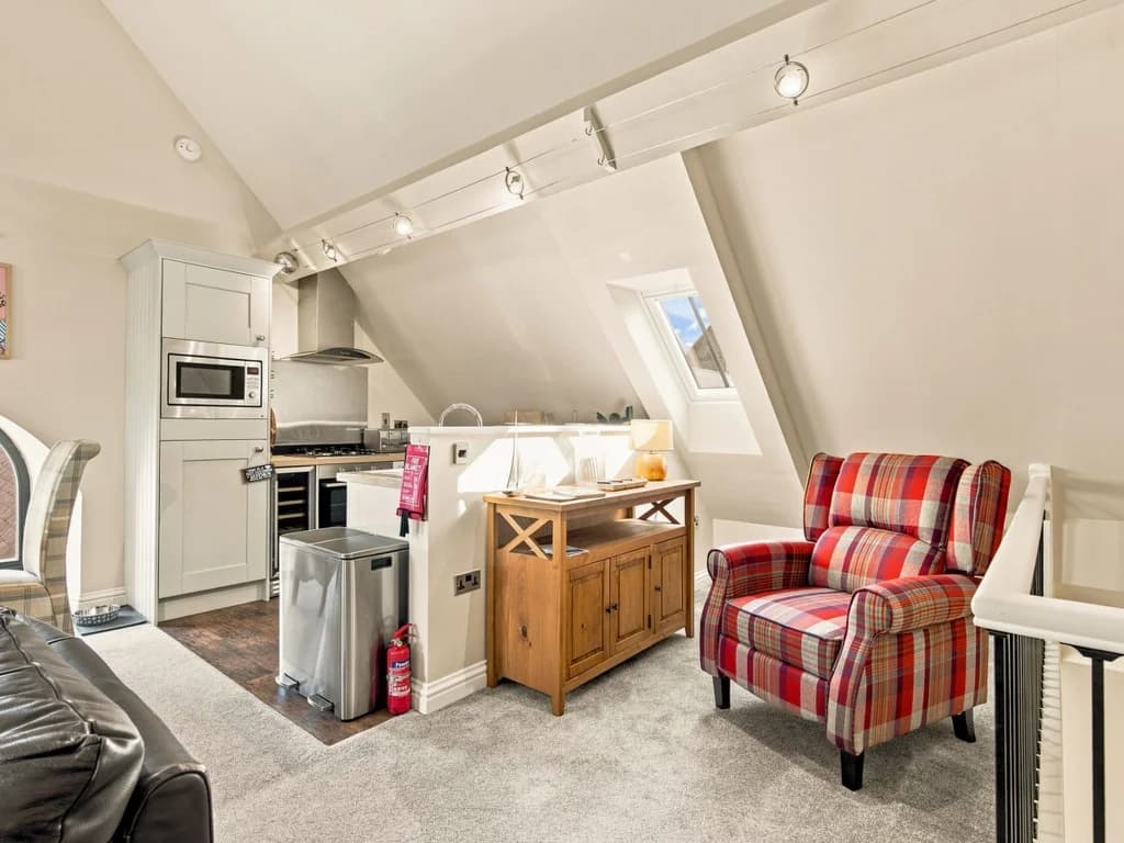 Comfortable lounge with tartan armchair and well-equipped kitchen beyond.