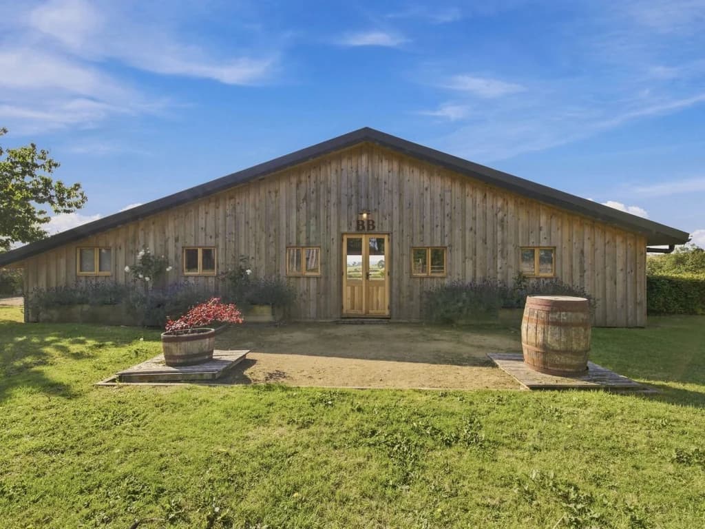 Timber-clad barn entrance framed by planters and established greenery