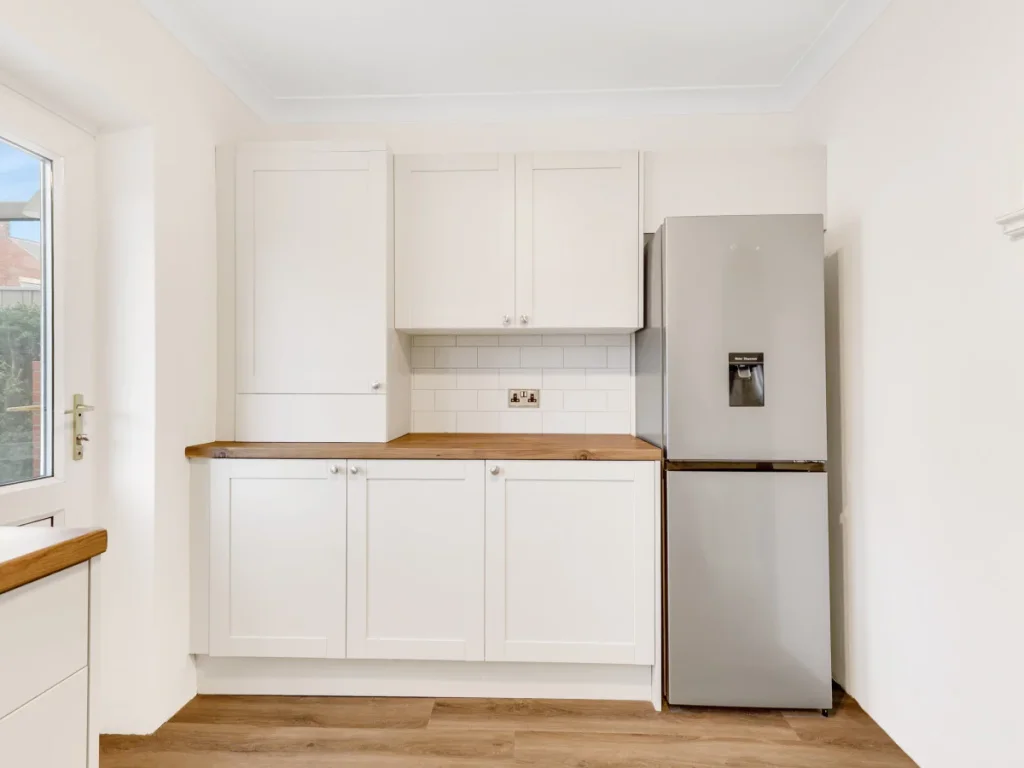 White fitted kitchen with fridge freezer, wood worktops and storage