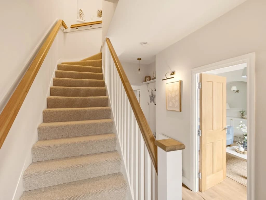 Carpeted staircase with wooden handrail leading to the first floor